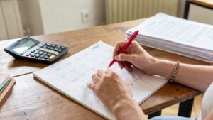 Donna segna un calendario cartaceo accanto a calcolatrice e fogli